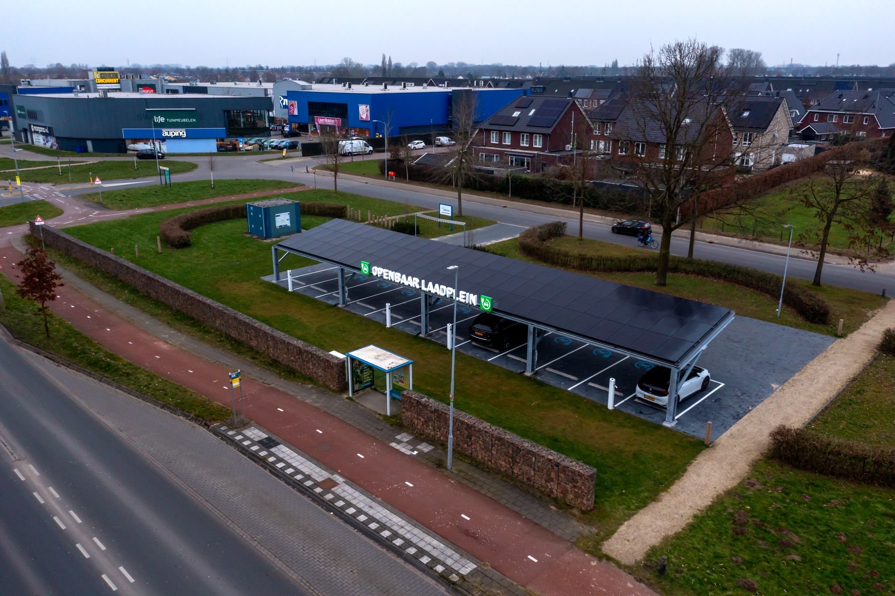 Dronefoto van Openbaar Laadplein Wijnbergen: overdekte laadplekken met zonnepanelen, met de woonboulevard op de achtergrond